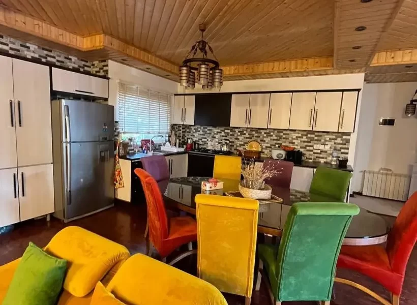 میزغذاخوری با صندلی های رنگی و یخچال و کابینت های سفید آشپزخانه در باقرتنگه