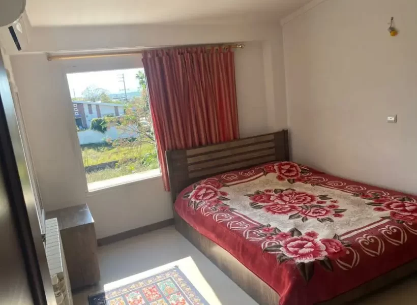 تخت با پتوی قرمز و پنجره با پرده ی صورتی اتاق خواب آپارتمان در پل سفید