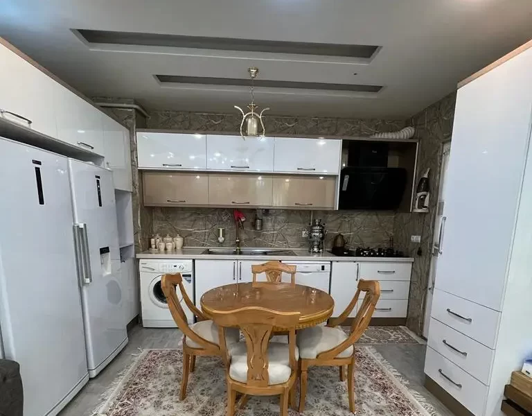 میز غذاخوری و یخچال و کمد و لباسشویی و کابینت سفید آشپزخانه آپارتمان در زرگر