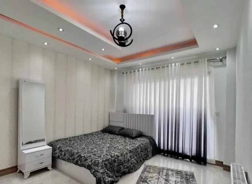 تخت خواب با روتختی سفیدمشکی و پرده سفید و سقف نور پردازی شده با نور نارنجی اتاق خواب ویلا در بابلسر