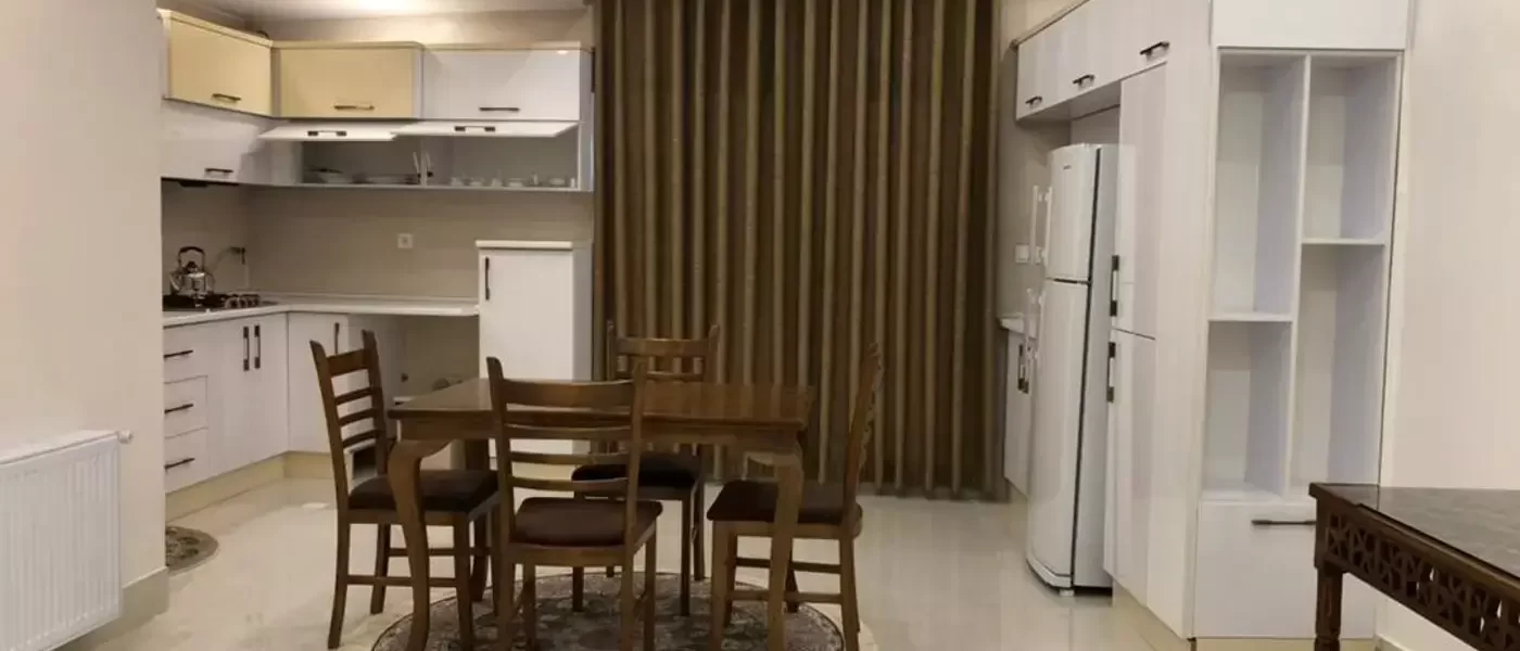 میز غذا خوری و کابینت های سفید و سقف نور پردازی شده با نور زرد و سفید آشپزخانه آپارتمان در قائم شهر