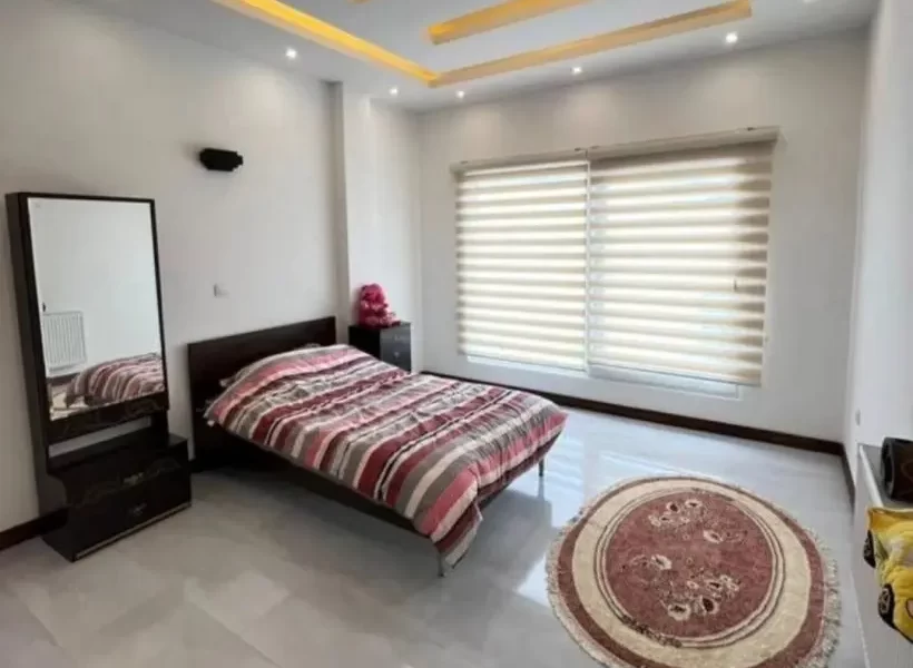 تخت خواب با روتختی رنگی و آیینه آرایش و سقف نور پردازی شده با نور زرد اتاق خواب ویلا در سوادکوه