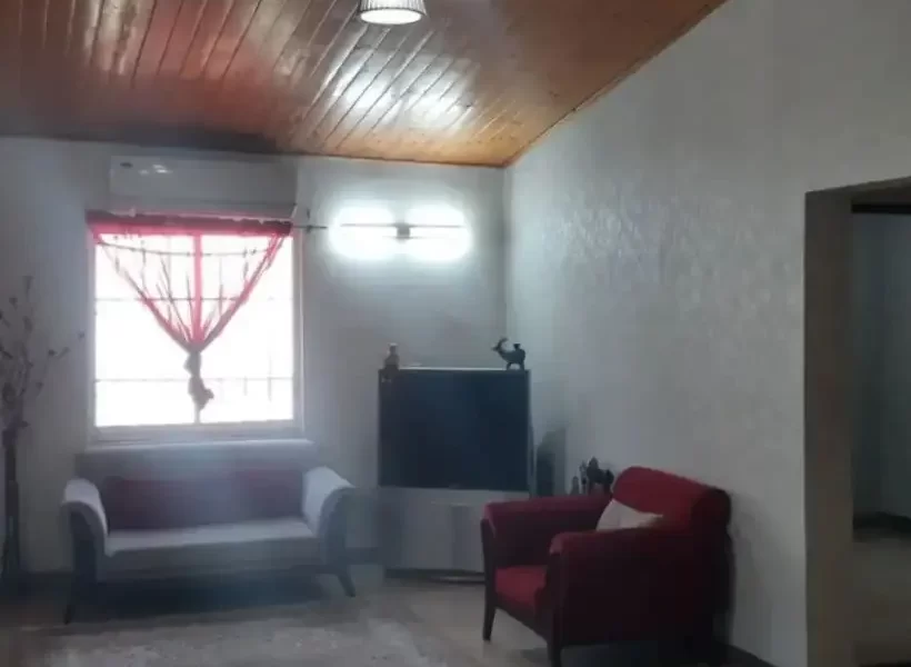 مبلمان قرمز و سفید و تلویزیون سالن نشیمن خانه روستایی در باقرتنگه