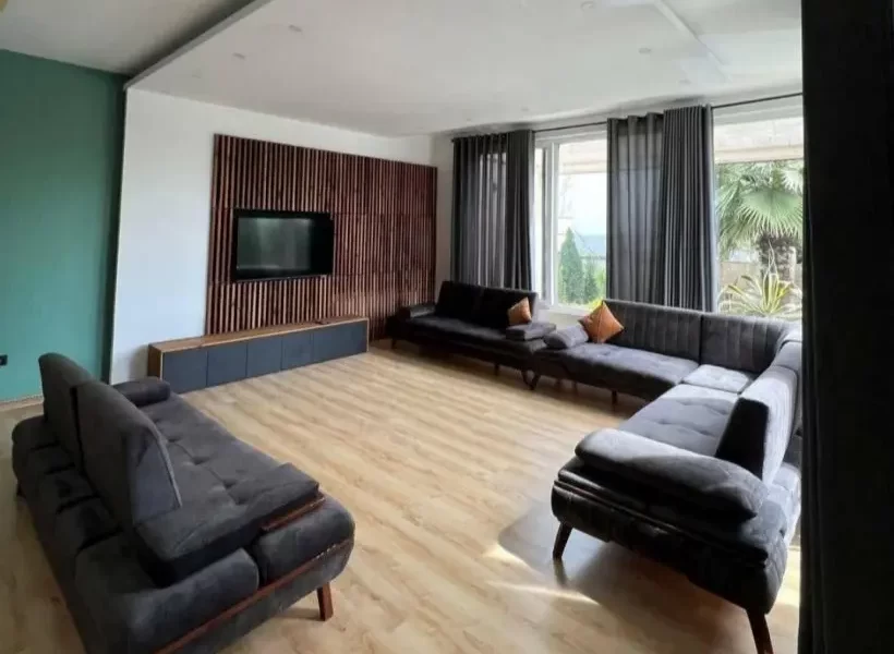 مبلمان مشکی رنگ و پنجره بزرگ رو به محوطه سرسبز سالن نشیمن ویلا در بابل