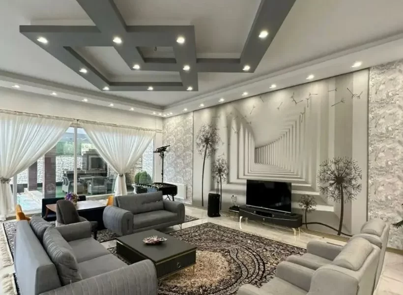 مبلمان طوسی و سفید رنگ و پنجره رو به محوطه سرسبز سالن نشیمن ویلا در بابل