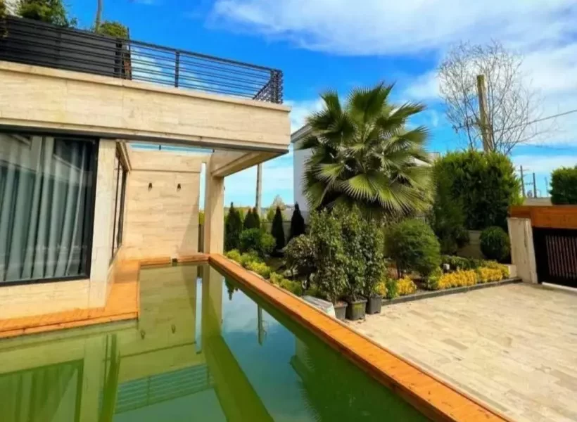 محوطه سنگ فرش شده و باغچه سرسبز و استخر محوطه ویلا در بابل